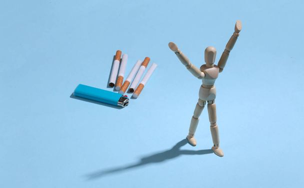 Raucherentwöhnung. Freiheit Holzpuppe auf blauem Hintergrund mit Zigaretten und Feuerzeug - Foto, Bild