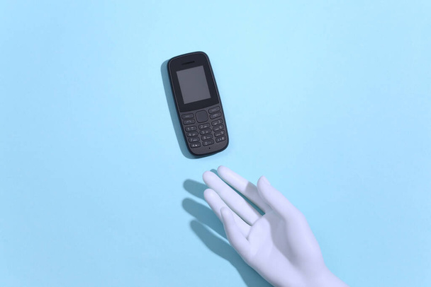 Ruka figuríny drží tlačítko telefonu na modrém pozadí. Horní pohled - Fotografie, Obrázek
