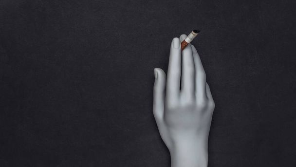 Mannequin hand holding cigarette on black background - Photo, image