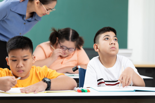 Ασιατικά παιδιά με ειδικές ανάγκες ή αυτισμός παιδιά που μαθαίνουν κοιτώντας και γράφοντας σε γραφεία με δασκάλους που βοηθούν στην τάξη - Φωτογραφία, εικόνα