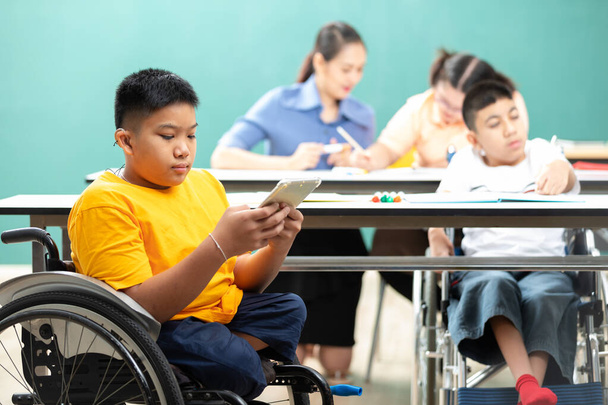 азіатські діти з обмеженими можливостями (втрачені ноги) використовуючи планшет і сидячи на інвалідному візку в класі
 - Фото, зображення