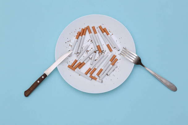 Sok cigaretta tányéron villával és késsel a kék háttéren. Felülnézet - Fotó, kép