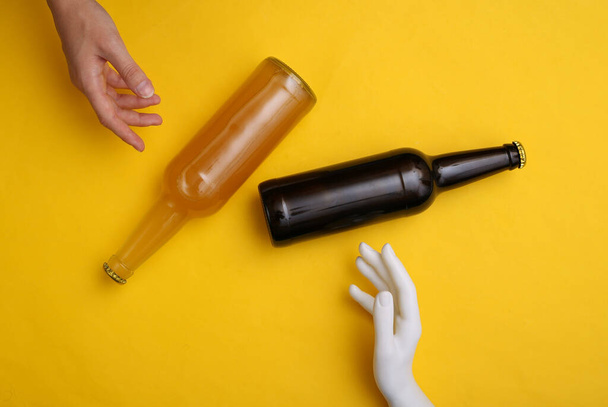 Human and mannequin hand touching beer bottle on yellow background - Foto, Imagen