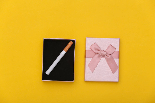 Cadeaudoosje met een sigaret op een gele achtergrond. Bovenaanzicht - Foto, afbeelding