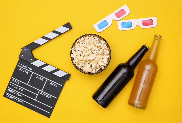 Movie time. Popcorn, beer bottles, movie clapper, 3d glasses on yellow background. Top view. Flat lay - Photo, Image