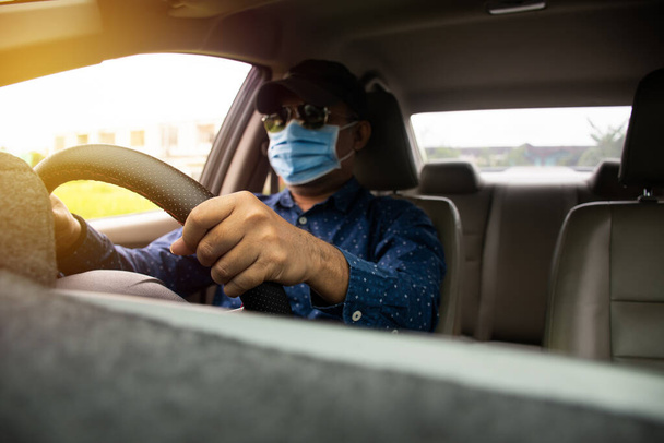 Een wazige man met een masker, een zwarte bril en een zwarte hoed. Sluit een man rijden handen om het stuur te houden om de auto zorgvuldig te controleren, terwijl de verkeersopstoppingen daglicht. Wazige achtergrond - Foto, afbeelding