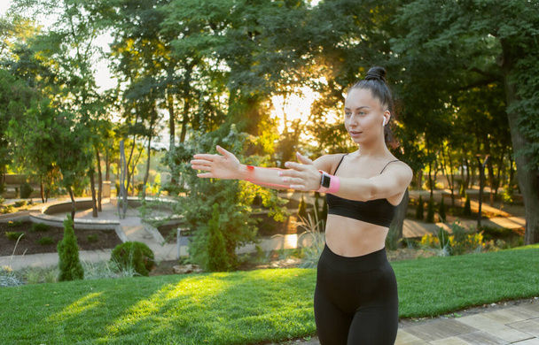 Young attractive brunette woman in sportswear exercises with fitness rubber bands in the park at sunrise - Photo, Image