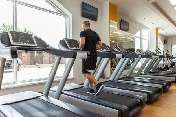 Jóképű izmos férfi testépítő gyakorol egy futópadon egy modern edzőteremben. Kardio edzés - Fotó, kép