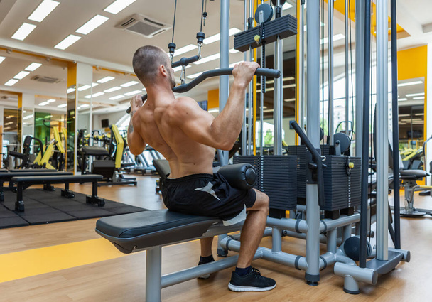 Fitness uomo muscoloso con busto nudo che lavora in macchina esercizio pulldown lat in palestra - Foto, immagini