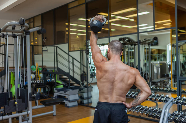 Treino-focado musculoso esculpido homem exercitando-se com um kettlebell no ginásio moderno. Treinamento de força de musculação - Foto, Imagem