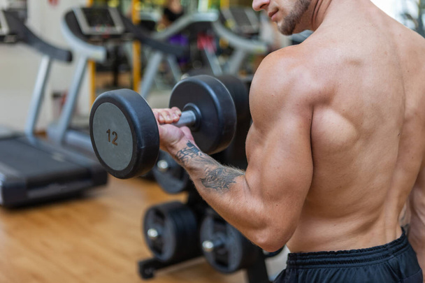 Geconcentreerd op training gespierde mager man oefenen met halters in de moderne fitnessruimte. Biceps pompen - Foto, afbeelding