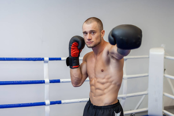 Hombre musculoso con un torso desnudo entrena puñetazo de mano con guantes de boxeo en el ring - Foto, Imagen