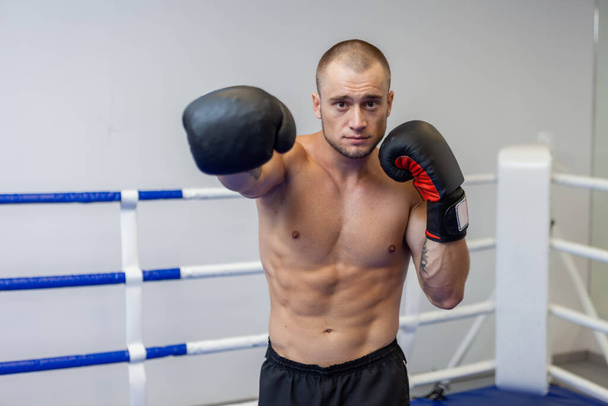 Мускулистый мужчина с обнаженным туловищем тренирует удар рукой в боксёрских перчатках на ринге - Фото, изображение