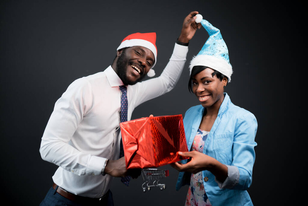 African american man in a red hat holding a gift with a woman in a blue christmas hat - Φωτογραφία, εικόνα