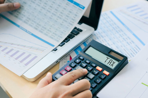 Close up Businessman and partner using calculator and laptop for calculating finance, tax, accounting, statistics, and analytic research concept. Tax word on a calculator. Business and tax concept. - Photo, Image