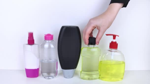 Frascos aislados de detergentes sobre fondo blanco. La mano toma los frascos de detergentes. En la foto, champú, agua micelar, jabón líquido y enjuague bucal. Productos químicos domésticos en recipientes de colores - Metraje, vídeo