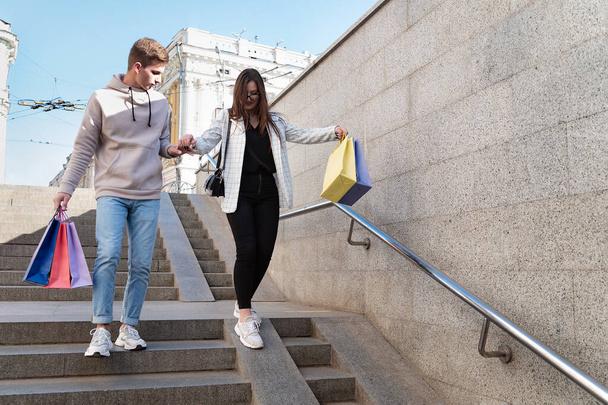 A turisták a városban sétálgatnak vásárlással a kezükben. A fickó segít a lánynak lemenni a lépcsőn.. - Fotó, kép