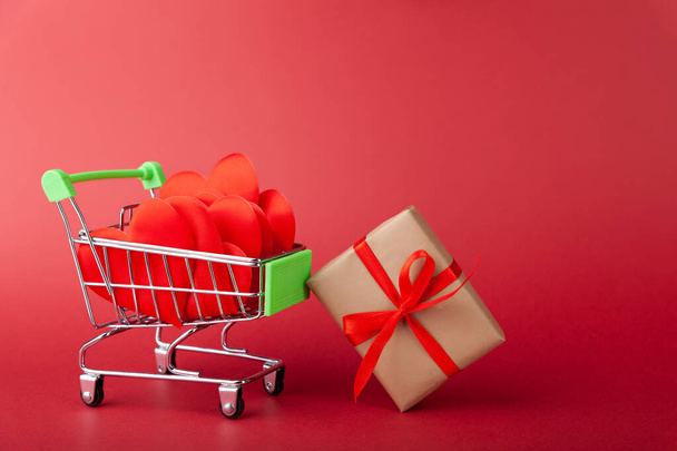 Red heart, gift box with red ribbon inside mini grocery cart on colored background - Fotografie, Obrázek