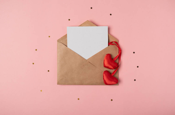 Craft envelope with a blank sheet of paper inside and red hearts on the rose background. Romantic love letter for the Valentine's day concept. Space for text. - Foto, Imagen