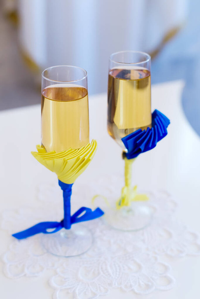 Twee bruiloft glazen met champagne voor paar met blauwe en gele linten decoratie  - Foto, afbeelding