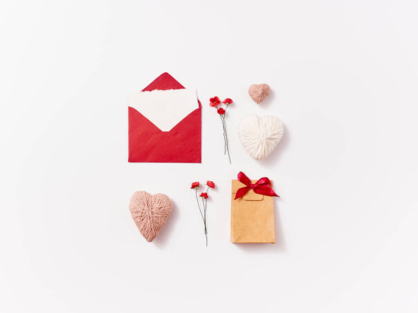 Composición plana de la postal laica del sobre hecho a mano, regalo, corazones, rosas y plumas para la tarjeta de felicitación sobre fondo blanco con espacio de copia - Foto, Imagen