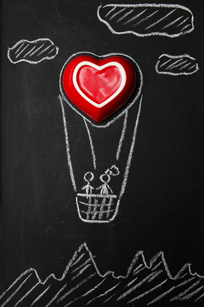 Un couple amoureux vole en montgolfière. Grand dessin coeur rouge avec craie blanche sur un tableau noir. Photo romantique pour la Saint-Valentin. Carte postale de félicitations. - Photo, image