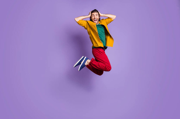 Full length photo portrait of man holding head with two hands jumping up isolated on vivid violet colored background - 写真・画像