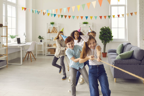 Bunch of happy multiethnic children playing tug-of-war at fun party at home or in kids club - Foto, Bild