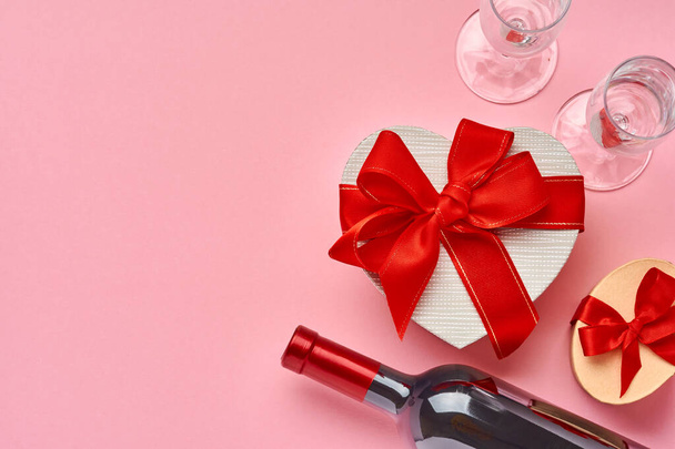 Wine, glasses and gift box in the form of heart with a red ribbon on pink background. Valentines day concept postcard. Top view. - Foto, immagini