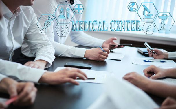 A group of doctors in a modern clinic is planned. The concept of modern medicine and medical biotenology. Medical icons on the screen with the inscription: MEDICAL CENTER - 写真・画像