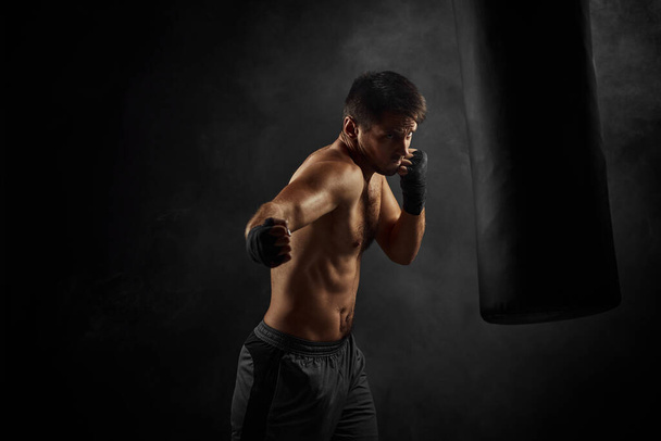 Male boxer punching in boxing bag on black background - Foto, immagini