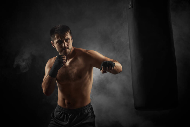 boxer in black boxing wraps punching in boxing bag - Valokuva, kuva