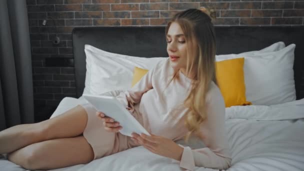vidám nő pihen az ágyban, és használja a digitális tabletta a szállodai szobában - Felvétel, videó