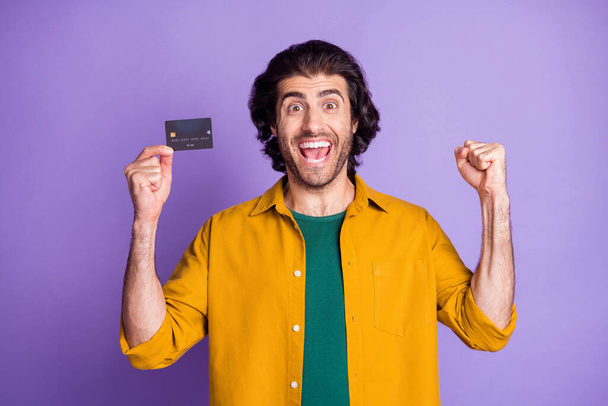 Photo portrait of celebrating man holding plastic card in one hand isolated on vivid purple colored background - Φωτογραφία, εικόνα