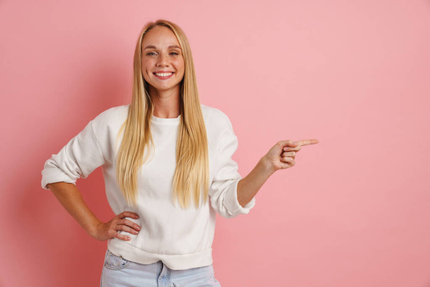 Happy beautiful girl smiling and pointing finger aside isolated over pink background - Фото, зображення