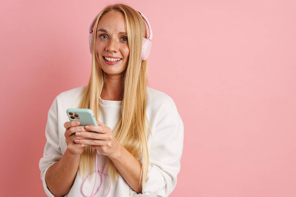 Happy beautiful girl listening music with headphones and cellphone isolated over pink background - Fotoğraf, Görsel