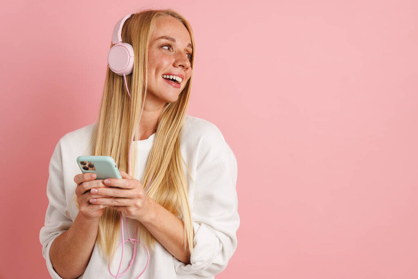 Happy beautiful girl listening music with headphones and cellphone isolated over pink background - Valokuva, kuva