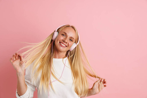Happy beautiful girl listening music with headphones and dancing isolated over pink background - Foto, Imagen