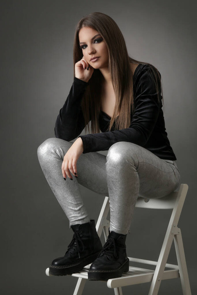 Fashion portrait of brunette woman in black shirt and silver leather leggings, studio shot. - Photo, image