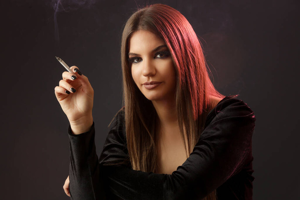 Studio portrait of young brunette woman with cigarette on dark background, looking at camera - Foto, immagini