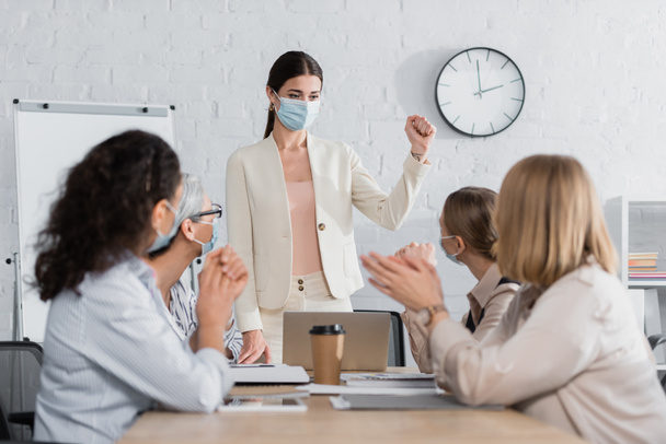 young team leader in medical mask standing with clenched fist interracial businesswomen on blurred foreground  - 写真・画像