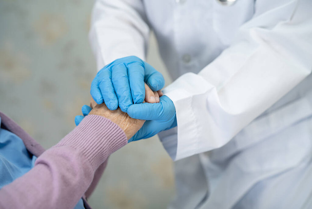 Arzt hält Hand einer asiatischen Patientin mit blauem Handschuh und Schutzanzug für Covid-19 Coronavirus. - Foto, Bild