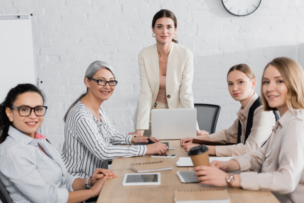 Teamleiterin steht bei Treffen im Amt neben glücklichen multiethnischen Geschäftsfrauen  - Foto, Bild