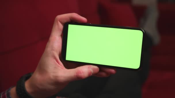 Close-up man handen houden chromakey groene scherm smartphone kijken inhoud, vegen scrollen op de bank thuis. Begrip "gadgets". - Video