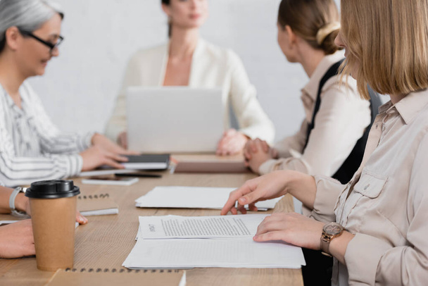 mujer de negocios cerca de contrato en el escritorio durante la reunión y compañeros de trabajo en segundo plano  - Foto, imagen