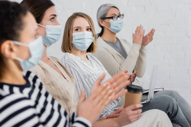 empresarias multiétnicas con máscaras médicas aplaudiendo durante el seminario en la sala de reuniones - Foto, imagen