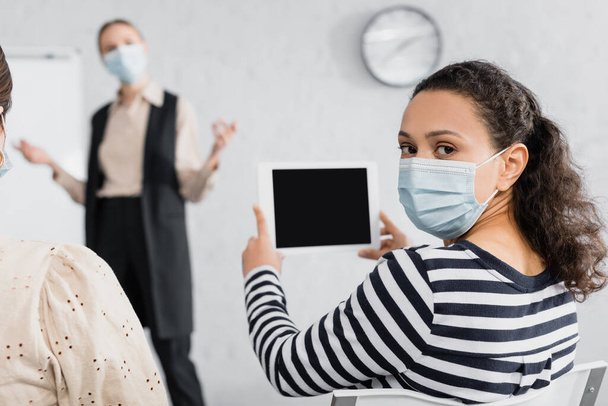 African american woman in medical mask holding digital tablet with blank screen near speaker  - Фото, изображение