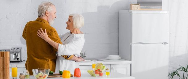 Positives älteres Paar umarmt reifes Gemüse auf Küchentisch, Transparent  - Foto, Bild
