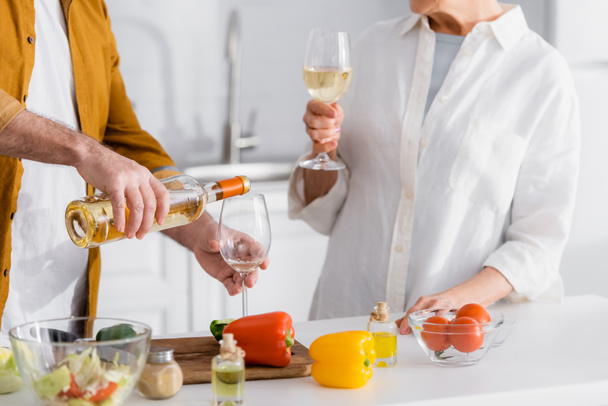 Cropped view of man pouring wine near wife and vegetables on blurred foreground  - Photo, image