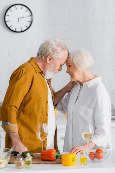 Sonriente coupé de edad avanzada abrazos cerca de vino y verduras en primer plano borrosa - Foto, imagen